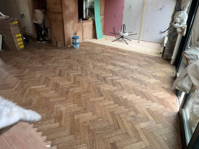 Oak herringbone parquet blocks being laid across a room during installation